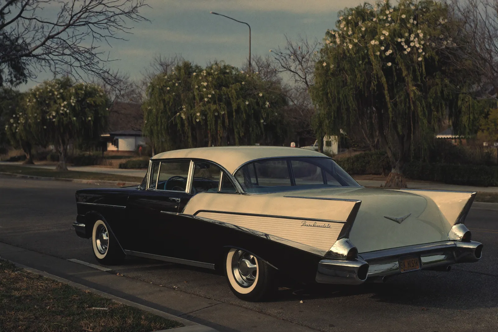 AI-generated illustration: a black-over-ivory 1957 Chevrolet Bel Air with chrome tail fins on an empty tree-lined boulevard in morning light.