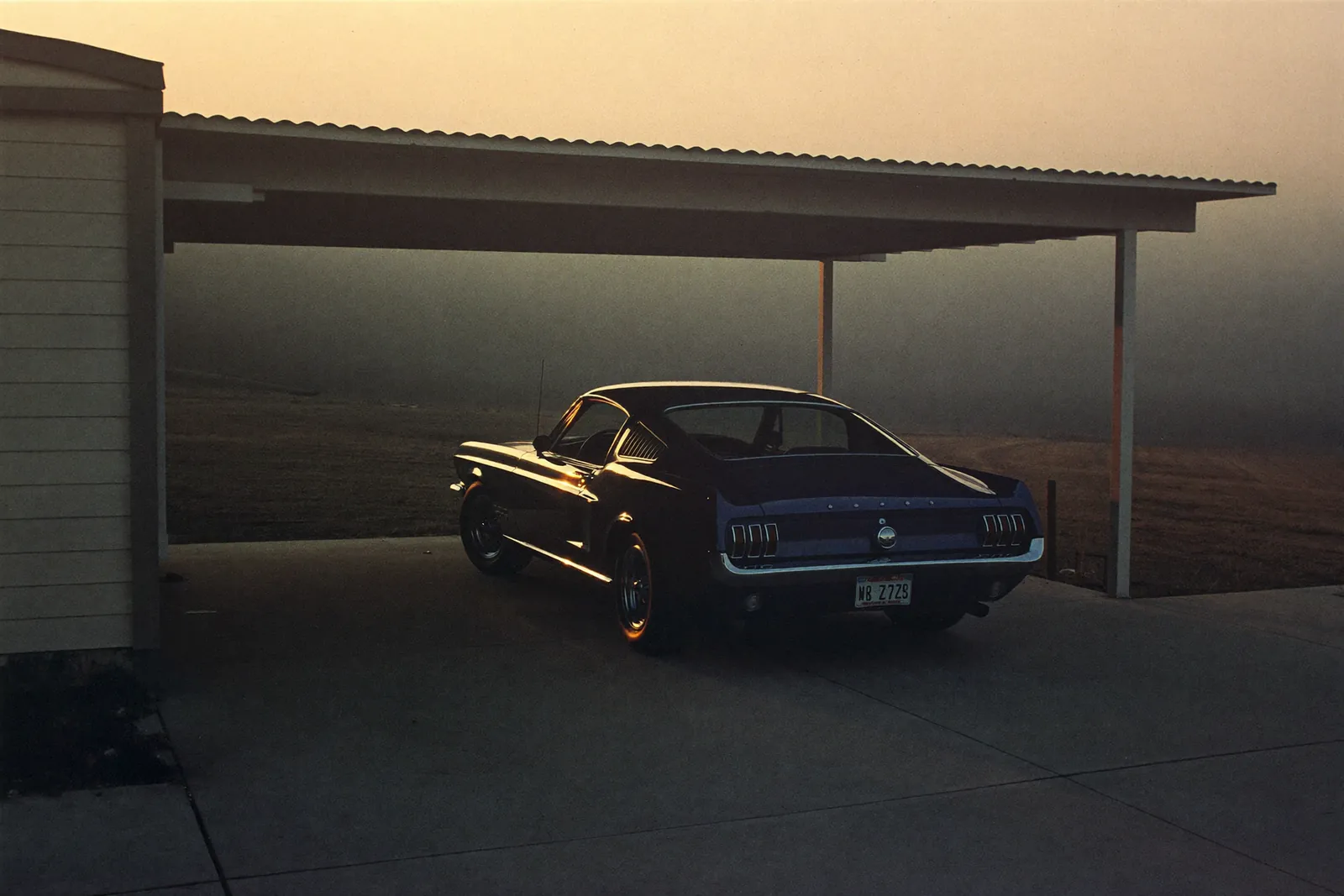 AI-generated illustration: a dark blue 1967 Ford Mustang fastback parked under a carport at dusk, long shadows on the driveway.